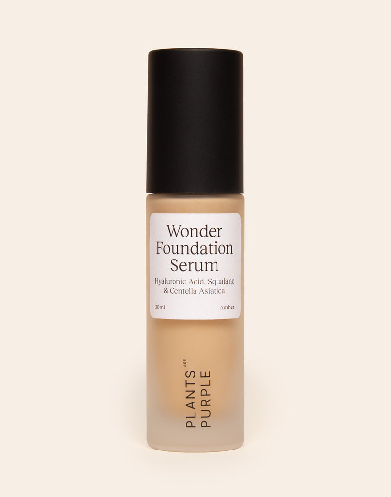 Bottle of Wonder Foundation Serum with black cap on a beige background.